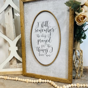 May include: A framed wooden sign with a white background and a black oval containing the text "I still remember the days I prayed for the things I have now".