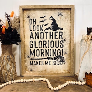 Pode incluir: Um sinal de Halloween emoldurado com um chapéu de bruxa e morcegos em um fundo vintage. O sinal diz "Oh look, another glorious morning! Makes me sick!"