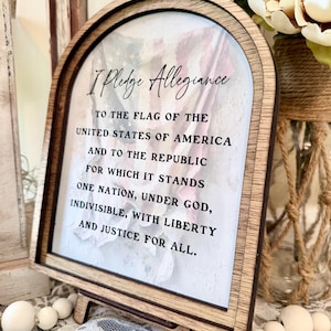 Peut inclure: Panneau encadré en bois avec le texte "I Pledge Allegiance" et l'intégralité du serment au drapeau des États-Unis d'Amérique. Le panneau est présenté sur un petit chevalet en bois, avec un fond floral.