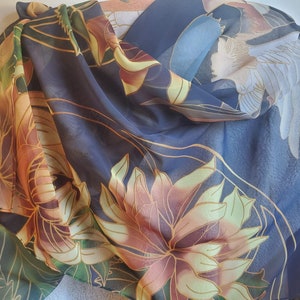 May include: A navy blue silk scarf featuring a floral and crane design. The flowers are in shades of yellow, orange, and brown. The crane is white with a blue head and neck.