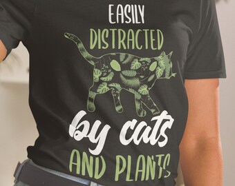 May include: A black t-shirt with a green cat and plant design. The text on the shirt reads "Easily Distracted by cats and plants".