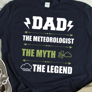 Könnte beinhalten: Ein marineblaues T-Shirt mit weißem Text, der "DAD", "THE METEOROLOGIST", "THE MYTH" und "THE LEGEND" lautet. Der Text wird von Wetter-Icons begleitet.