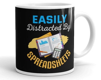May include: A black coffee mug with a white rim and handle. The mug has a graphic of a notebook, pencil, and calculator with the text "EASILY Distracted By SPREADSHEETS".