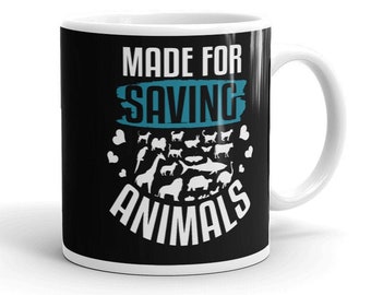 Könnte beinhalten: Eine schwarze Kaffeetasse mit weißem Rand und Henkel. Die Tasse hat ein weißes Motiv mit verschiedenen Tieren, umgeben von Herzen, und den Text "Made for Saving Animals" in Weiß und Blau.