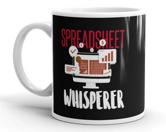 May include: White ceramic mug with a black background and red text that reads "Spreadsheet Whisperer". A computer monitor icon with a checkmark, dollar signs, and a bar graph is displayed above the text.