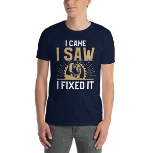 May include: A navy blue t-shirt with a white graphic that says "I came I saw I fixed it". The graphic also features a cartoon image of a person using a saw.
