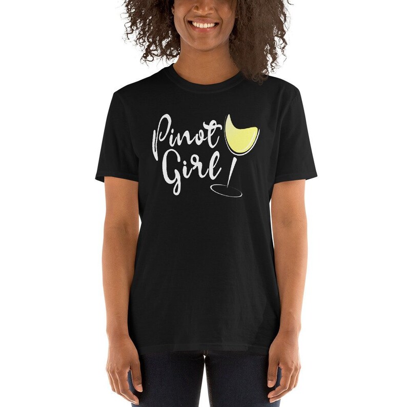 以下が含まれることがあります： 白い文字で「Pinot Girl！」と書いてある黒い半袖Tシャツ。白いワインのグラスのグラフィックが描かれている。