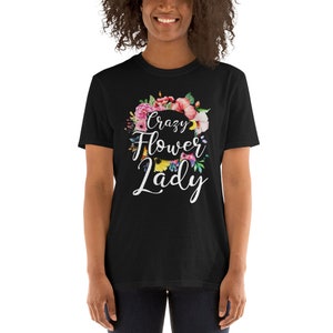 May include: Black t-shirt with the text "Crazy Flower Lady" in white script, surrounded by a colorful floral wreath. The flowers include pink, red, and yellow blooms. The shirt is a short-sleeved crew neck.