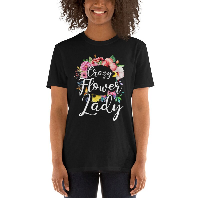 May include: Black t-shirt with the text "Crazy Flower Lady" in white script, surrounded by a colorful floral wreath. The flowers include pink, red, and yellow blooms. The shirt is a short-sleeved crew neck.