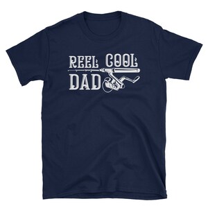 May include: Navy blue t-shirt with the text "REEL COOL DAD" in white, featuring a fishing rod and reel graphic. The shirt is a short-sleeved crew neck.