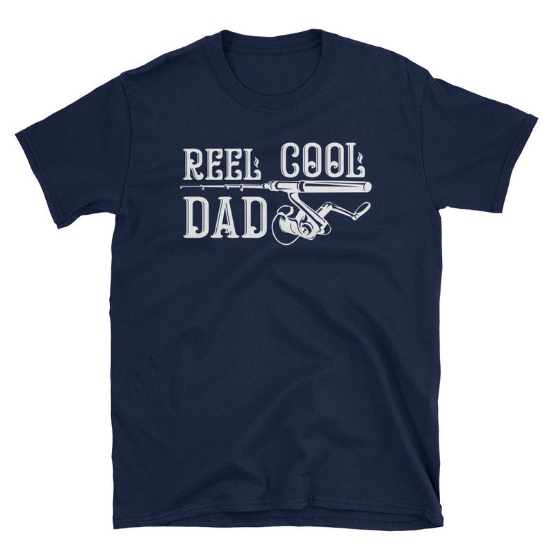 May include: Navy blue t-shirt with the text "REEL COOL DAD" in white, featuring a fishing rod and reel graphic. The shirt is a short-sleeved crew neck.