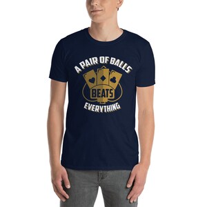 May include: A navy blue t-shirt with a white graphic design. The graphic features three playing cards with the text "A Pair of Balls Beats Everything".
