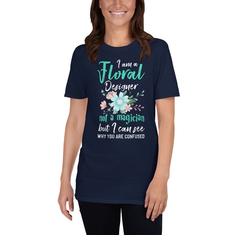 May include: Navy blue t-shirt with a floral design and the text "I am a Floral Designer not a magician but I can see why you are confused".