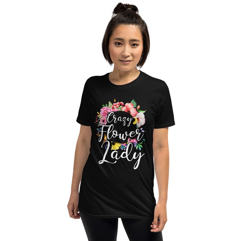 May include: Black t-shirt with the text "Crazy Flower Lady" in white script, surrounded by a floral wreath of pink, red, and yellow flowers. The shirt is a short-sleeved crew neck.