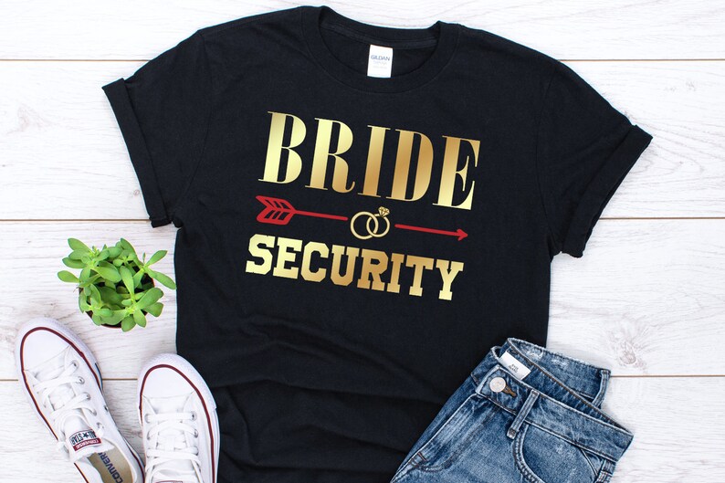 May include: Black t-shirt with gold text that reads "Bride Security" and a red arrow with gold rings.