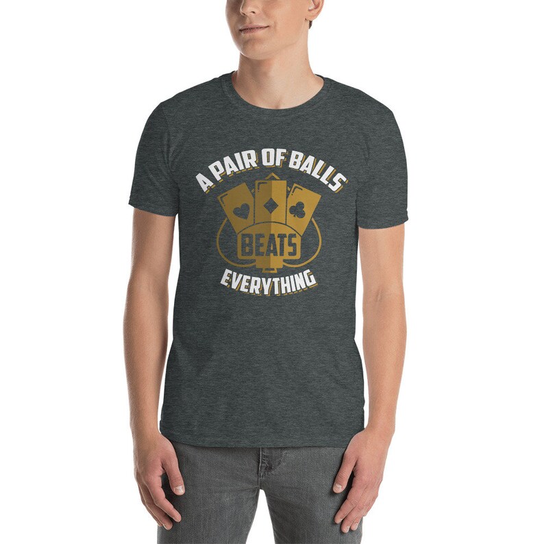 May include: A dark heather grey t-shirt with a white graphic design that says "A Pair of Balls Beats Everything". The graphic features three playing cards in a diamond shape with the words "Beats Everything" in the center.