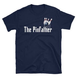 May include: A navy blue t-shirt with a white graphic of bowling pins and a bowling ball. The text "The Pinfather" is printed in white below the graphic.