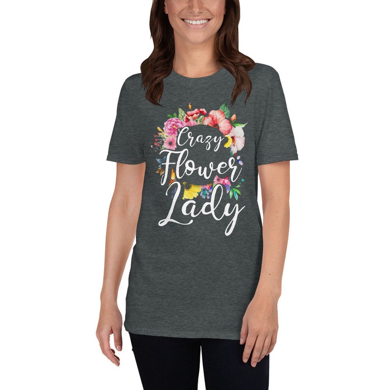 May include: Dark gray t-shirt with the text "Crazy Flower Lady" in white script, surrounded by a floral wreath of pink, red, and yellow flowers. The shirt is a crew neck and short-sleeved.