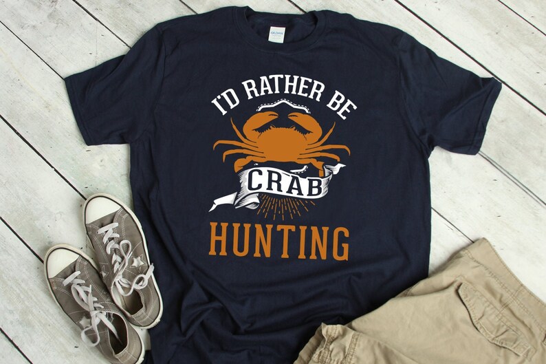May include: A navy blue t-shirt with the text "I'd rather be crab hunting" in white and orange. A cartoon crab is featured in the design.