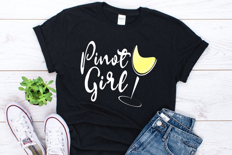 以下が含まれることがあります： 「Pinot Girl!」という白い文字と黄色のワイングラスのグラフィックが描かれた黒いTシャツです。