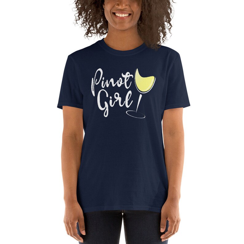 以下が含まれることがあります： 白い筆記体で「Pinot Girl!」と書かれたネイビーブルーのTシャツと、白い輪郭の白ワイングラス。