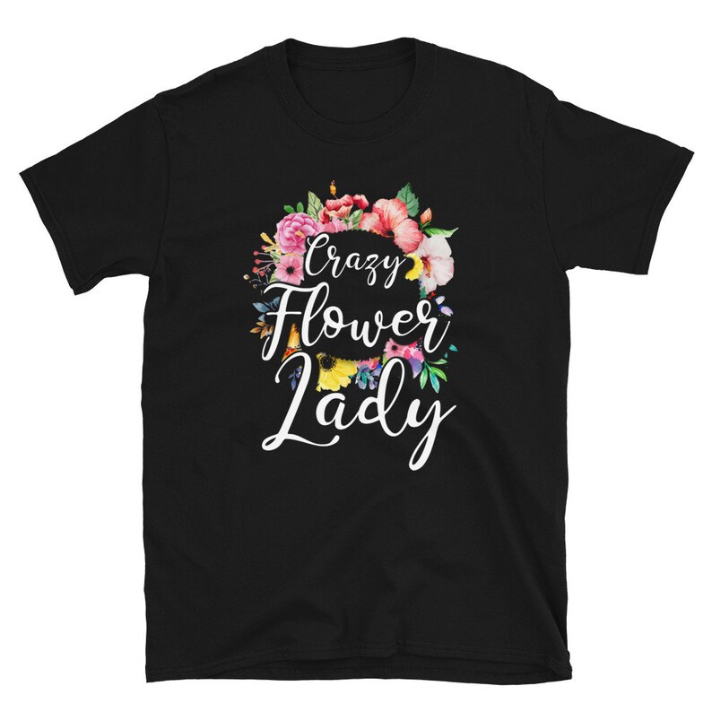 May include: Black t-shirt with a floral wreath design and the words "Crazy Flower Lady" in white script. The wreath features pink, red, and yellow flowers with green leaves. A casual tee for flower enthusiasts.