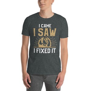 May include: A dark heather grey t-shirt with a white graphic that says "I came I saw I fixed it". The graphic also features a cartoon image of a person using a saw to cut wood.
