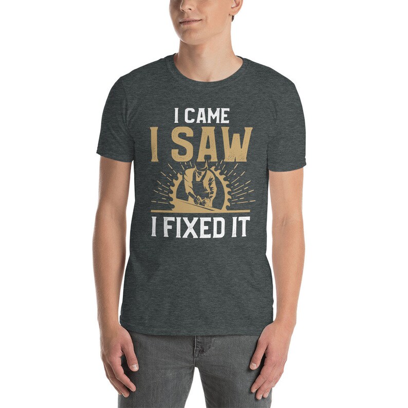 May include: A dark heather grey t-shirt with a white graphic that says "I came I saw I fixed it". The graphic also features a cartoon image of a person using a saw to cut wood.
