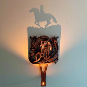 May include: A wooden wall sconce with a light that casts a shadow of a person riding a horse on the wall. The sconce is made of intricate, carved wood and has a warm, inviting glow.