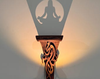 May include: A wooden wall sconce with intricate Arabic calligraphy carvings. The sconce casts a shadow of a person sitting in a meditative pose.