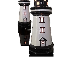 May include: Two decorative lighthouse lamps. The lamps are white with black accents and a black top. The lamps have rectangular windows that emit a warm glow. The lighthouses are a nautical theme.