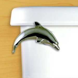 May include: A chrome-plated dolphin toilet paper holder. The dolphin is leaping up and over the edge of a white toilet tank.