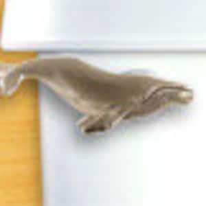 Może przedstawiać: Srebrny gałka do szafki w kształcie ogona wieloryba z detalicznym wzorem. Wieloryb jest zwrócony w prawo i ma lekko otwartą paszczę.