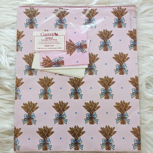 K&ouml;nnte beinhalten: Eine Packung pinkfarbenes Geschenkpapier mit Weizenmotiv, blauen Schleifen und wei&szlig;en Geschenkkarten. Die Packung enth&auml;lt 22 Geschenkpapierb&ouml;gen im Format 61 cm x 76 cm und 23 Geschenkkarten und Umschl&auml;ge im Format 7,6 cm x 10,2 cm. Der Text auf der Packung lautet "Current WHEAT Everyday Gift Wrap 22 24-by-30 Gift Wrap Sheets 23 3-by-4 Gift Cards & Envelopes CODE 1754 COLORADO SPRINGS, CO 80911"