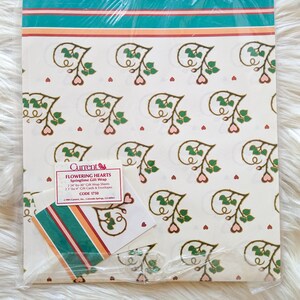 K&ouml;nnte beinhalten: Eine Packung wei&szlig;es Geschenkpapier mit einem Blumenmuster aus rosa Herzen und gr&uuml;nen Bl&auml;ttern. Das Papier ist mit "Flowering Hearts Springtime Gift Wrap" beschriftet und hat die Code-Nummer 1750.