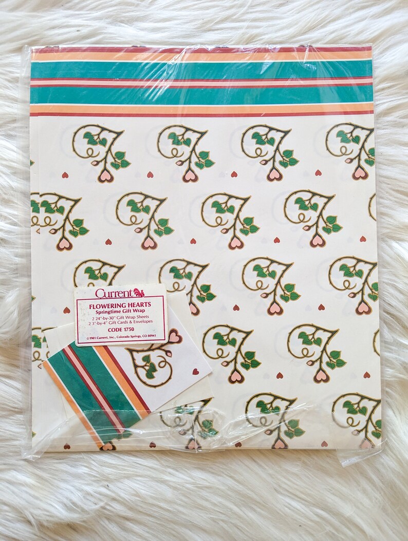 K&ouml;nnte beinhalten: Eine Packung wei&szlig;es Geschenkpapier mit einem Blumenmuster aus rosa Herzen und gr&uuml;nen Bl&auml;ttern. Das Papier ist mit "Flowering Hearts Springtime Gift Wrap" beschriftet und hat die Code-Nummer 1750.