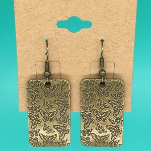 May include: A pair of gold-toned earrings with a rectangular shape and a butterfly design. The earrings have a hook closure.