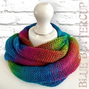 May include: A colourful knitted infinity scarf with a rainbow ombre pattern in shades of blue, green, yellow, orange, red and pink.