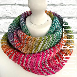 May include: A vibrant, knitted infinity scarf in shades of pink, orange, green, and purple. The scarf is displayed on a white mannequin head. The word "BLURBITTER" is written vertically on the right side of the image.