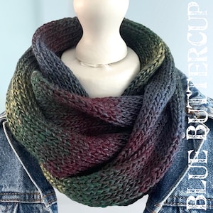 May include: A knitted infinity scarf in shades of green, blue, and purple. The scarf is made with a textured stitch and has a gradient colour pattern.