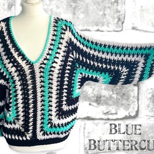 May include: A crocheted sweater with a v-neck and long sleeves. The sweater is black, white, and turquoise. The text "BLUE BUTTERCUP" is printed on the bottom right corner of the image.