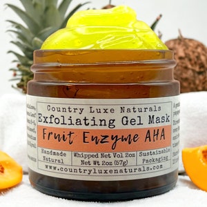 May include: A brown glass jar filled with a yellow gel mask. The label reads "Exfoliating Gel Mask Fruit Enzyme AHA." The jar is surrounded by papaya slices and a pineapple. The product is handmade and natural.