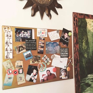 May include: A corkboard with a variety of photos, postcards, and inspirational quotes. The corkboard is decorated with a gold star and a wooden frame. The text on the corkboard includes "Be yourself. There is something that you can do better than any other. Listen to the inward voice and bravely obey that." and "Life isn't about finding yourself. Life is about creating yourself."