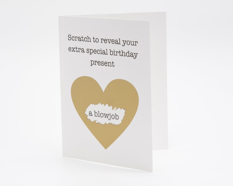 May include: A white birthday card with a gold heart-shaped scratch-off area. The text on the card reads "Scratch to reveal your extra special birthday present." The revealed message says "a blowjob."