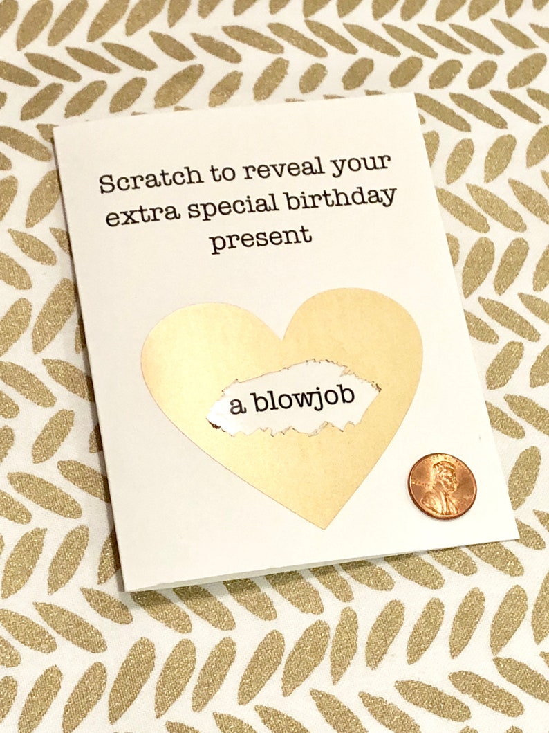 May include: A white greeting card with the text "Scratch to reveal your extra special birthday present." A gold heart shape has a scratch-off area revealing the words "a blowjob." A penny is next to the card.