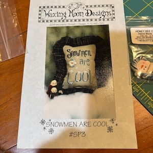 May include: A craft pattern from Waxing Moon Designs featuring a snowman-themed design. The image shows a small pillow with the words "Snowmen are Cool" and a decorative border. The pattern is labeled #SP3.