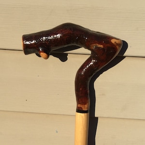 May include: A wooden walking stick with a dark brown, gnarled handle and a light brown shaft.