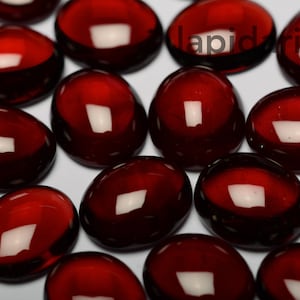 Könnte beinhalten: Eine Sammlung glatter, roter Glassteine. Die Steine sind oval geformt und haben eine glänzende Oberfläche.