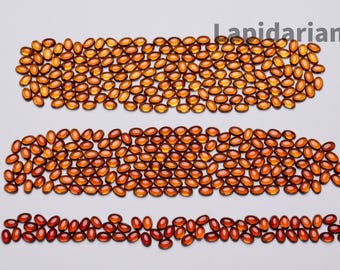 May include: Three rows of oval-shaped, amber-colored gemstones arranged on a white surface. The top two rows are a lighter amber, while the bottom row is a deeper, reddish-brown hue. The word "Lapidarians" is in the top right corner.