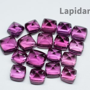 Könnte beinhalten: Eine Ansammlung quadratisch geschliffener, facettierter Edelsteine in tiefen Magenta- und Lilatönen. Die Edelsteine sind auf einer weißen Oberfläche angeordnet, mit dem Wort "Lapidarians" in grauem Text oben. Die Edelsteine haben eine polierte, reflektierende Oberfläche.